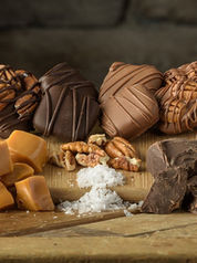 Assorted handmade chocolates and caramels topped with sea salt and pecans, arranged on a wooden board.