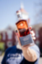 Person holding a bottle of Company Distilling Straight Bourbon Whiskey finished with maple wood, with the historic Lynchburg courthouse softly blurred in the background.