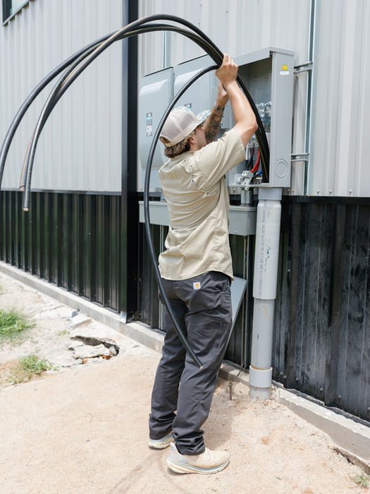 Electrician installs cables near a building's exterior, working on electrical system.