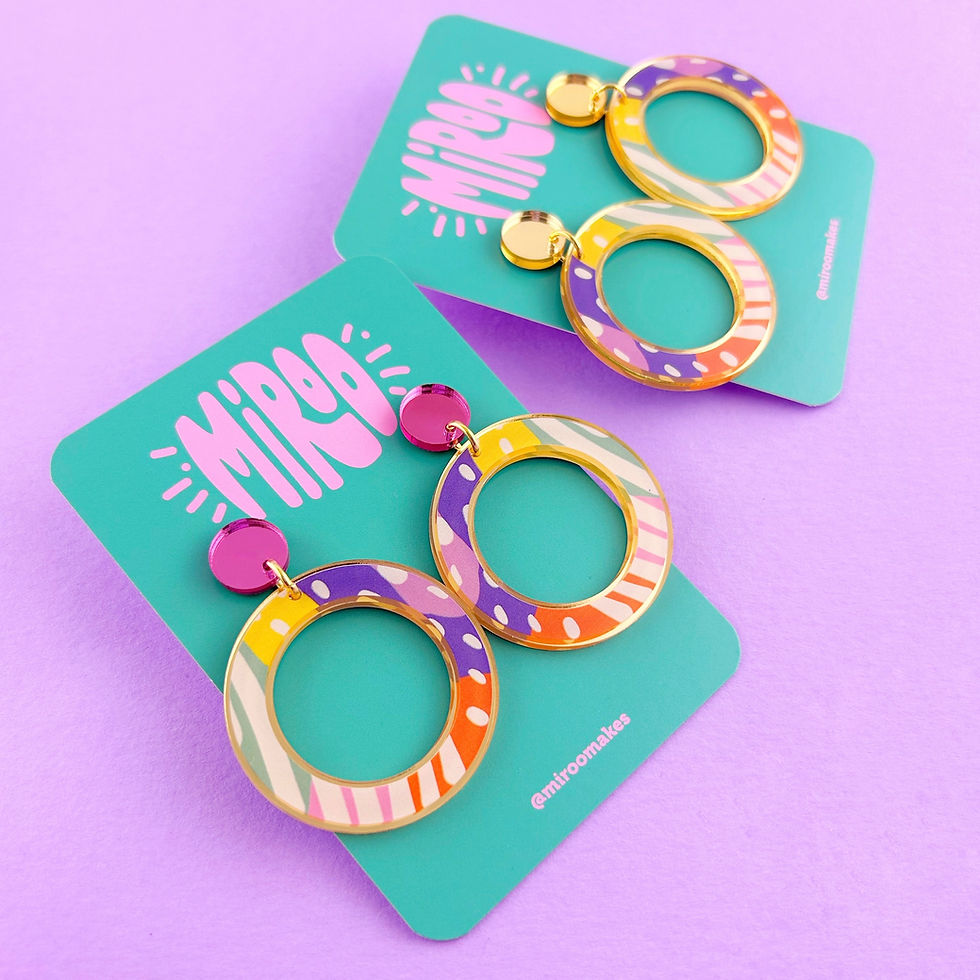 Thumbnail: A pair of large, circle shaped earrings. They have a fun and colourful pattern and the mirrored gold acrylic can be seen edge