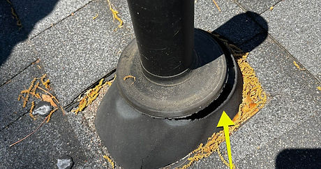 A close-up photograph of a rotten, cracked rubber pipe jack flashing on an asphalt shingle roof causing active water leaks