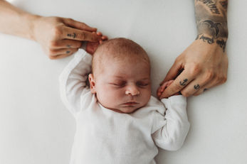 Tätowierte Hände der Mutter halten behutsam die Hände des schlafenden Babys –Newbornshootings zu Hause.