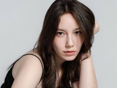 A professional headshot portrait of actor and model Hanna, featuring soft studio lighting against a clean, minimal light gray background.