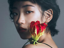 A close-up portrait of photographer Misuzu Shibuya, captured with a single red flower and dramatic lighting.
