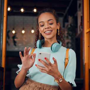 Person using a smartphone in a café setting, representing everyday customer engagement on WhatsApp as highlighted in the Genesys announcement.