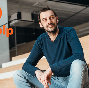 Man in blue shirt and jeans sits on wooden stairs, looking thoughtful. Infobip logo in orange is visible on the left. Industrial setting.