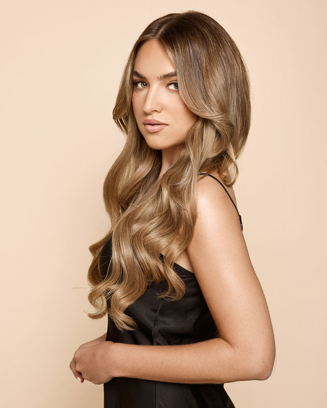 Woman with long wavy hair and black dress, E-COMMERCE/FASHION, standing against beige background. Jenia Ria