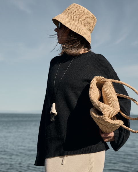 Woman wearing knit black sweater and white skirt holding a bag