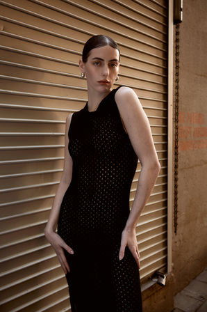 Woman in black crochet-knit dress posing against an urban corrugated metal shutter, knitwear lookbook photography