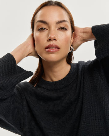 Woman poses with hands behind head, wearing black shirt. Jenia Ria