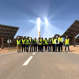 Render arquitectónico de una planta termosolar con una torre central y miles de espejos helióstatos rodeándola en el desierto de Baja California Sur bajo un cielo azul intenso, abril 2026.