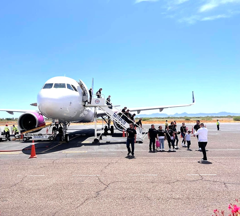 Pasajeros con maletas caminando por la moderna y renovada sala de espera del Aeropuerto Internacional de La Paz con grandes ventanales hacia la pista de aterrizaje.