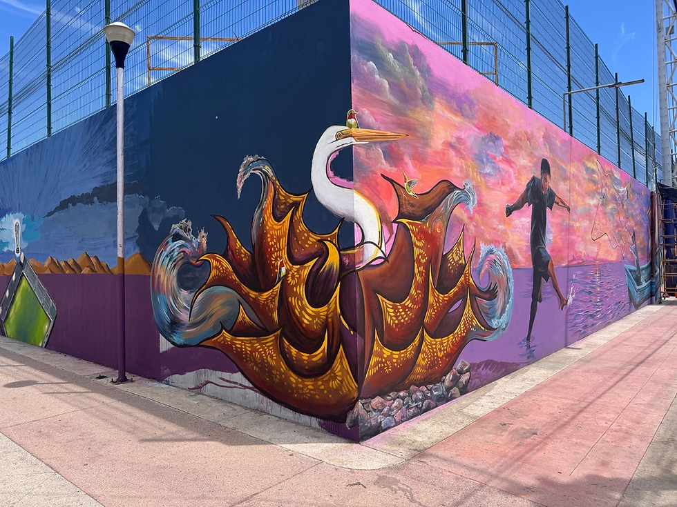 Artistas plásticos sudcalifornianos usando andamios y aerosoles de colores para pintar trazos de futbolistas y balones sobre una enorme pared urbana bajo el cielo azul de La Paz.
