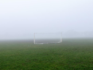 Un campo de fútbol municipal completamente encharcado y vacío, con las porterías solitarias bajo un cielo gris y lluvioso.