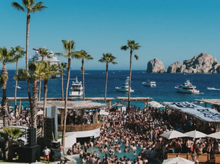 Young tourists enjoying the beaches of Cabo San Lucas during the 2026 Spring Break season, with active local businesses in the background.