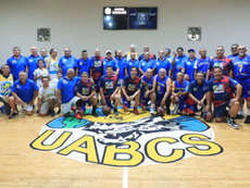 Veteran basketball players from UABCS Gatos Salvajes and Tec de La Paz Lobos Marinos posing together and embracing on the hardwood of the University Gymnasium.