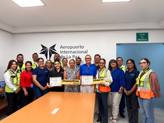 Desplastifícate award plaque displayed at the La Paz Airport terminal, with travelers in the background using reusable water stations.