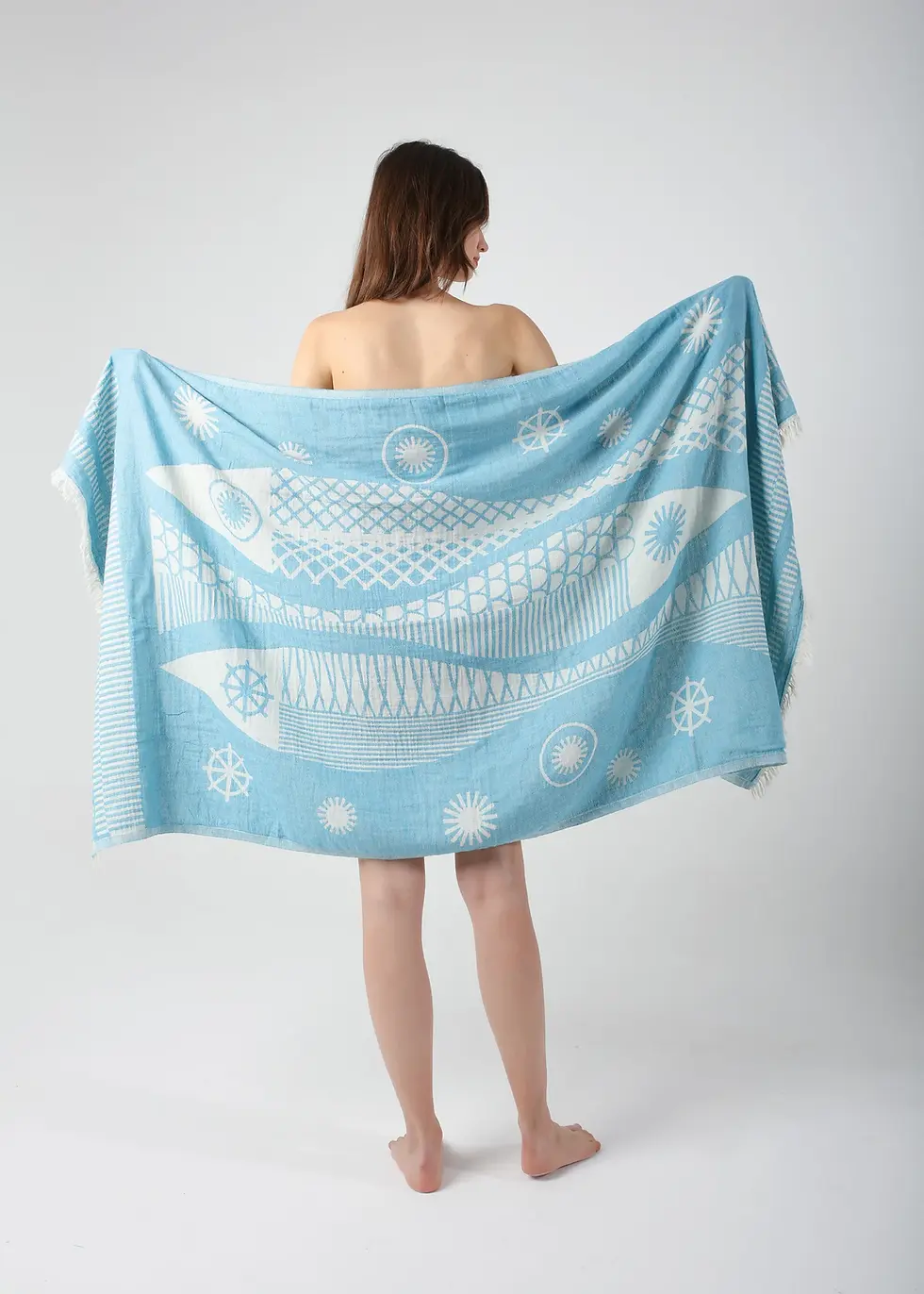 Thumbnail: Woman holds light blue Santa Barbara Turkish Towel with white design, Peshtemal Concept.