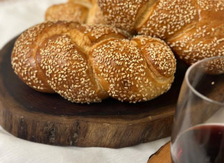 חלות שבת טריות על קרש חיתוך עץ לצד כוס יין אדום.