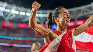 A triumphant female athlete wrapped in her national flag, celebrating passionately in a stadium after a hard-fought victory.
