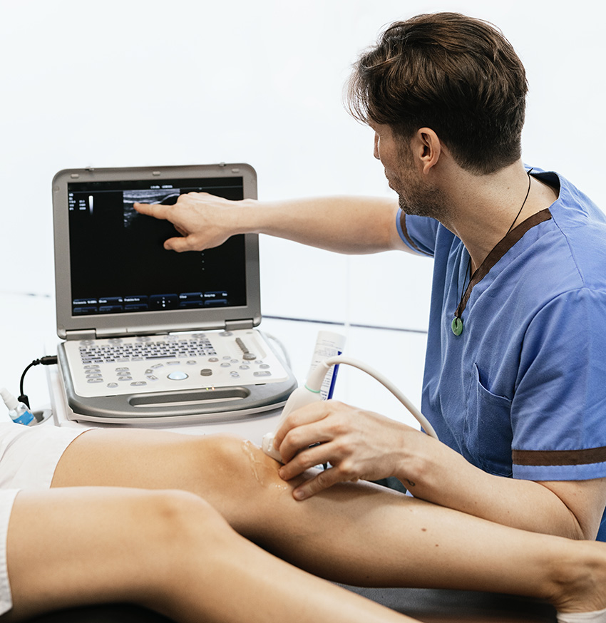 Clinician performing knee ultrasound and reviewing real-time imaging on the screen.