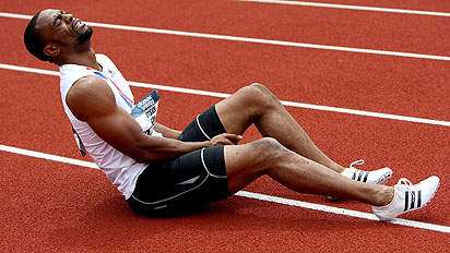 Track athlete clutching hamstring in pain during competition.