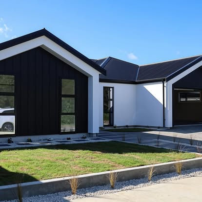 Modern newly built single-story home with a black and white exterior, featuring large windows, a double garage, landscaped front yard, and clean architectural lines under a clear blue sky.