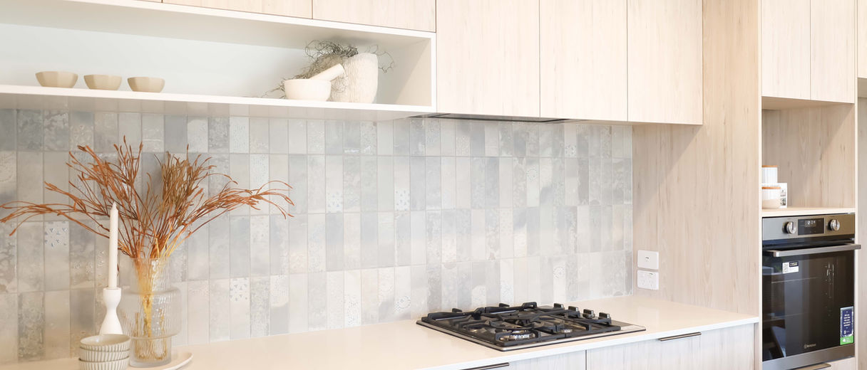 Modern light wood kitchen with gas cooktop, textured grey tile backsplash, built-in oven, and minimalist open shelving decor.