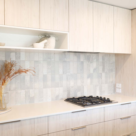 Modern light wood kitchen with gas cooktop, textured grey tile backsplash, built-in oven, and minimalist open shelving decor.