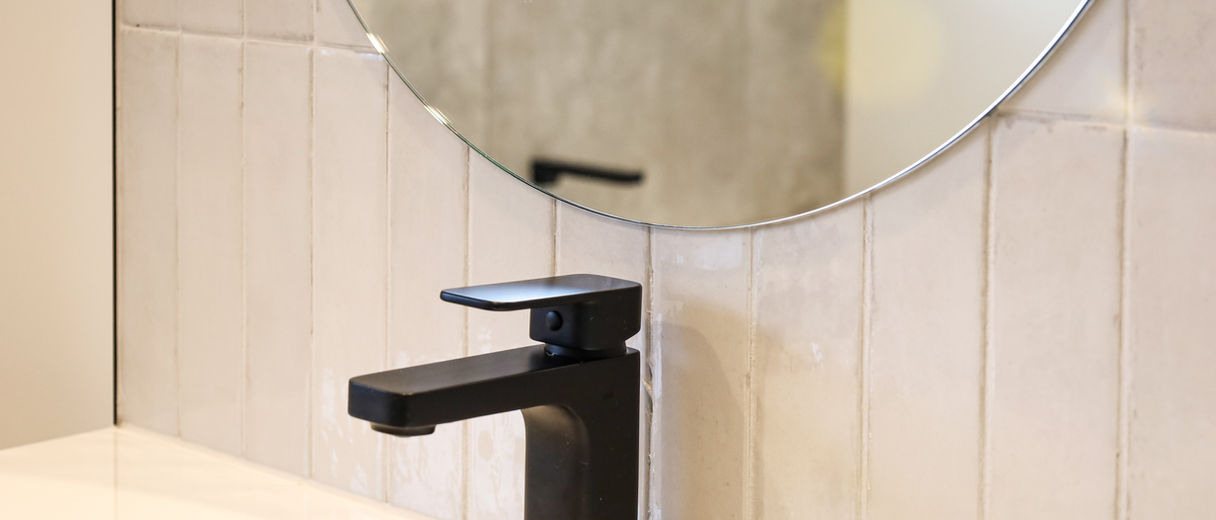 Modern black basin tap with round mirror and soft finger tiles.