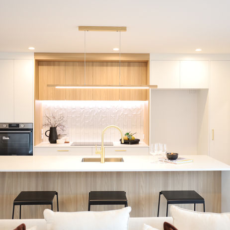 Contemporary kitchen design in custom-built home featuring a stone island benchtop, gold tapware, integrated cabinetry, timber accents, vertical tile splashback, and modern pendant lighting—perfect for showcasing high-end residential construction and craftsmanship.