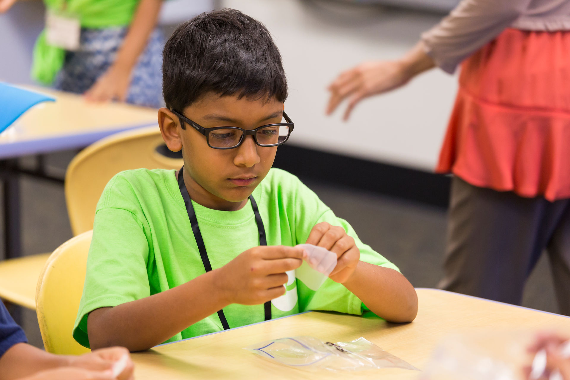 An India boy wearing a bright green t-shirt working on a science lab in class