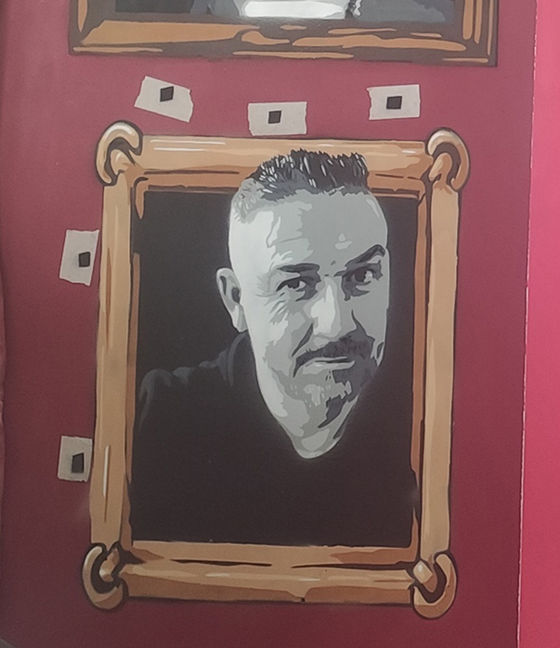 Retrato de um colaborador da Algarve Paint Store no mural, com a cara pintada em cinza e a moldura em castanho. Vê-se a fita cola com marcações para a colocação do próximo stencil, mostrando a fase de preparação.