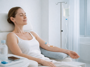 Woman in white tank top receiving IV therapy, relaxing with closed eyes in a bright, minimalist clinic. Water bottle and phone nearby.