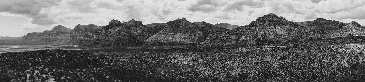 The image captures the dramatic landscape of Red Rock Canyon, with its rugged, red rock formations stretching across the horizon. The black and white photography emphasizes the stark beauty of the desert landscape, highlighting the texture and depth of the rocks. The interplay of light and shadow creates a sense of drama and mystery. The image evokes a feeling of awe and wonder, showcasing the power and majesty of nature.