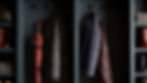 Muted closet with blue walls holds a red umbrella, two patterned jackets, folded gray towels, and red rain boots on shelves.