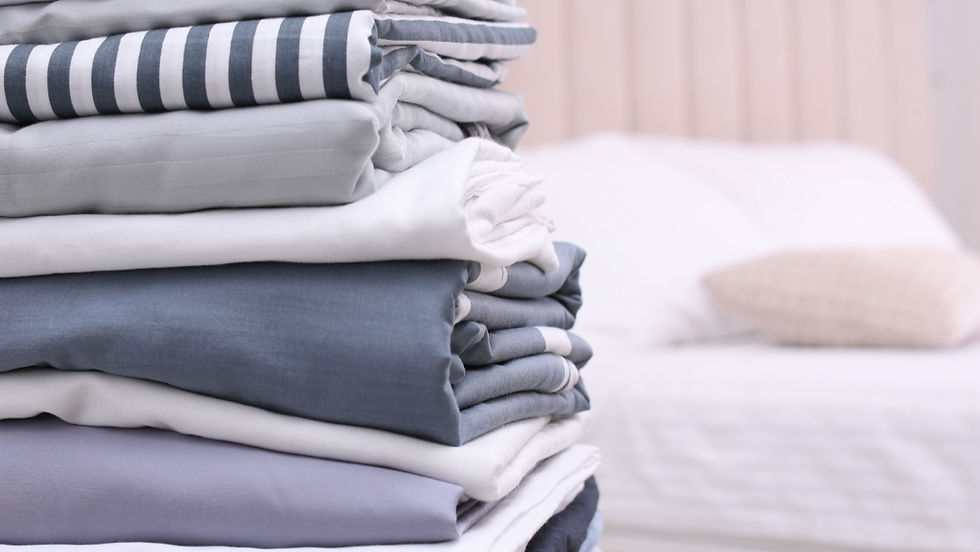 Stack of folded bed linens in blue, gray, and white stripes on a bed in a cozy bedroom. Calm and orderly atmosphere.