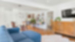 Bright modern organized living room with blue sofa, dining table, bookshelf, wall TV, plants, and wood cabinet on hardwood floor.
