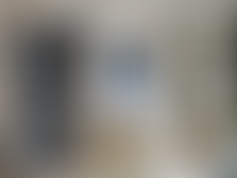 Glass cabinet with wine glasses, a cozy bed in a blue-walled room visible through a doorway, a beige sofa with cushions on the right. Organized downsized condo.