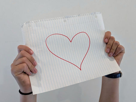 person holding up a paper with a heart drawn on it.