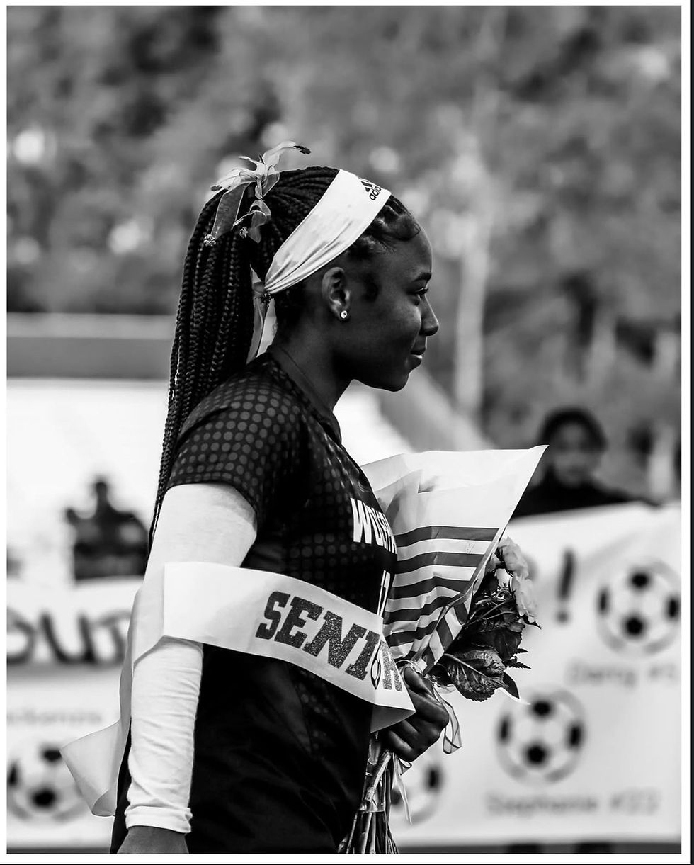 Young woman in profile with braids and headband holds flowers, wearing a "Senior" sash. Background shows soccer-themed decor.