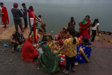 Women in colorful sarees performing traditional rituals with diyas and offerings by the riverside in India.