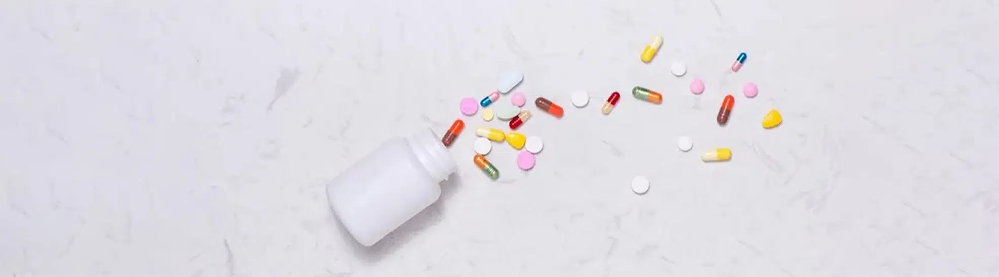 Pills spread on a white background with an empty pill bottle copy