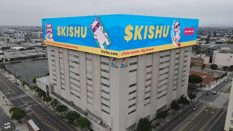 Large building with OOH advertising showing a vibrant blue billboard featuring cartoon dogs and text "$KISHU." Overcast urban setting, minimal street activity.