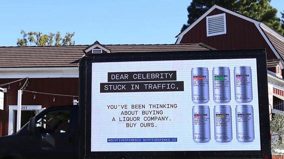 Truck with a billboard displaying text: "Dear celebrity stuck in traffic, buy our liquor company," colorful cans shown. Background has houses, trees, blue sky.