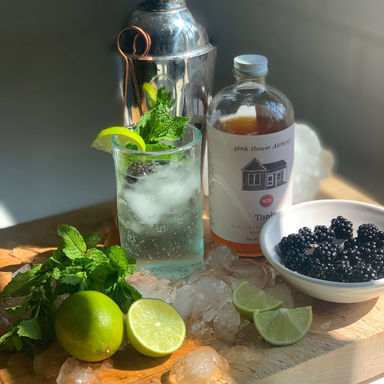 glass filled with fizzing clear cocktail, lime and blackberries on an ice covered cutting board with all the cocktail components