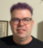 a headshot of Pastor Chris Becker. Chris has short purple hair, wears glasses, and has on a plain black t-shirt