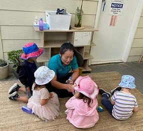 保育園で実習中のKCAの学生。4人の園児の前でお話をしている留学生