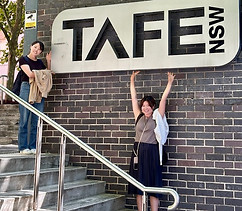 TAFE NSWの看板の前で笑顔でポージングをする留学生NozomiさんとFumikaさん。