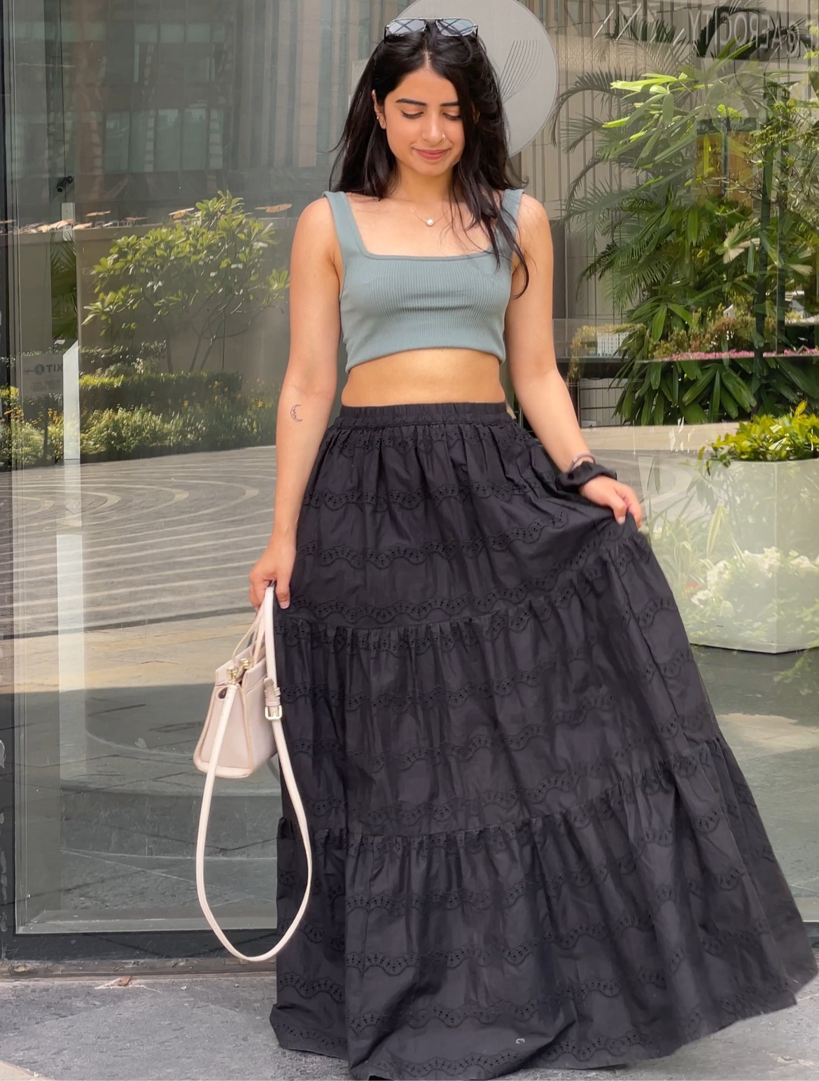A woman in a gray crop top and black tiered skirt, holding a beige handbag outdoors.